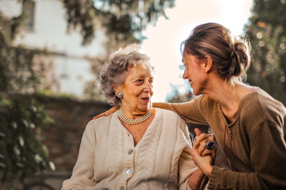 An older mum laughing with her adult daughter in a garden
