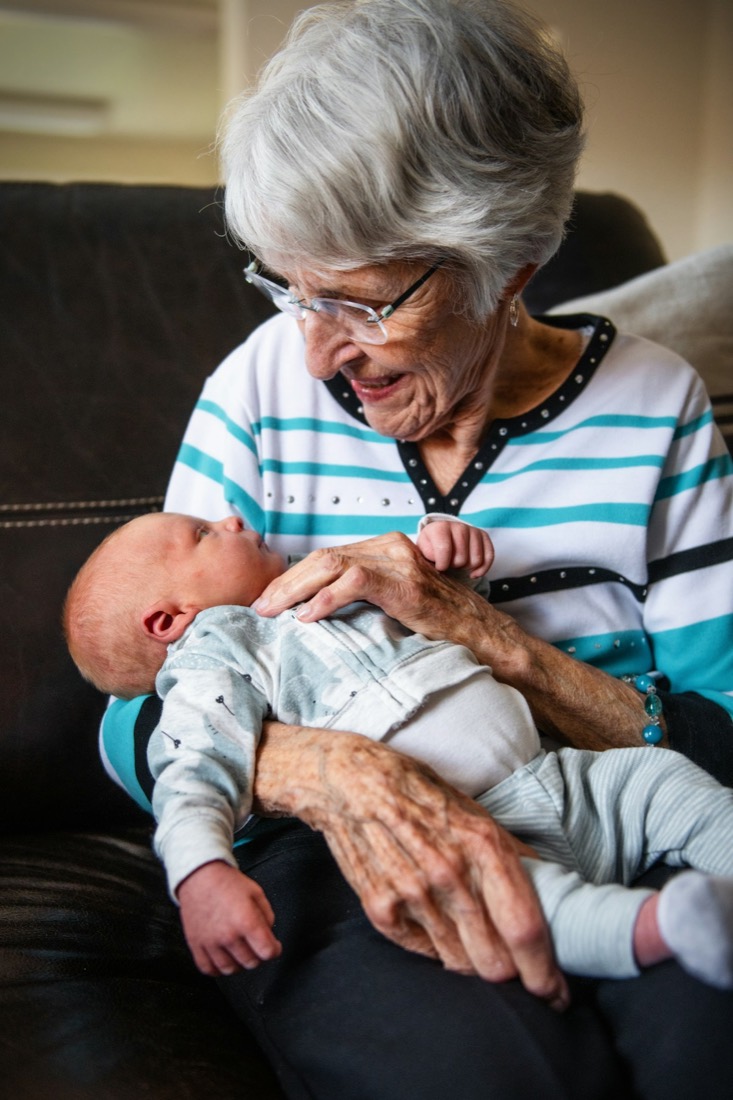 A great-grandmother smiling at a newborn baby in her arms